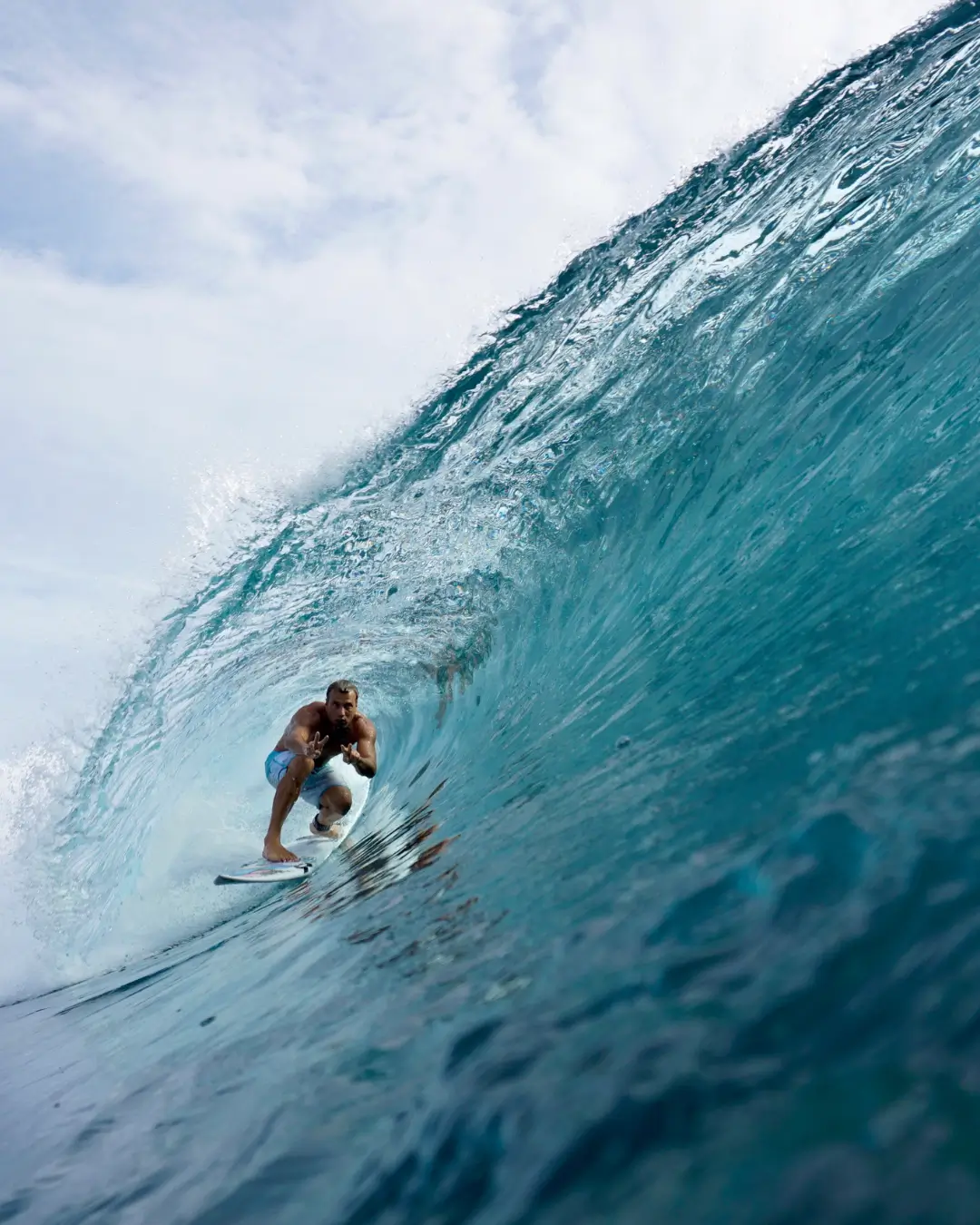 Surfers paradise in the mentawais - a man is surfing a wave, he is in between the curling wave and is holding up a peace sign with both hands